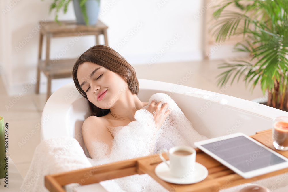 Beautiful young woman taking relaxing bath with foam at home