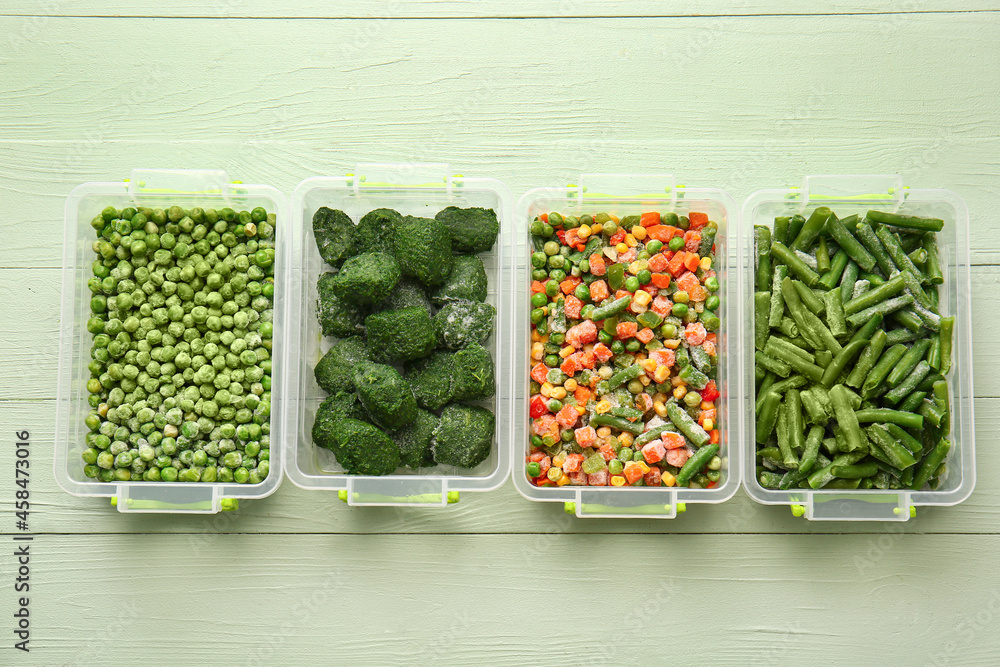 Plastic containers with different frozen vegetables on color wooden background