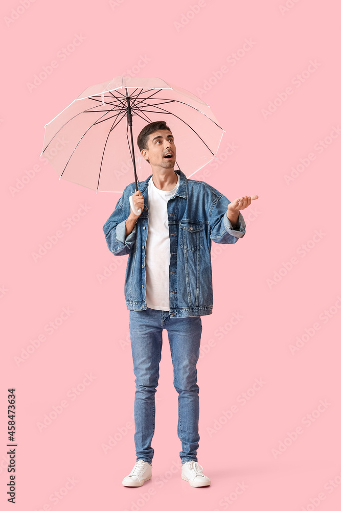Surprised young man with umbrella on color background