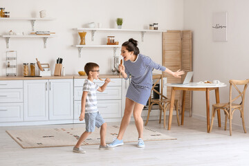 Wall Mural - Young woman and her little son dancing and singing in kitchen