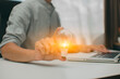 © aekachai - Businessman holding a bright light bulb on wooden table