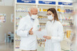 © Dusan Petkovic - Colleague advice. Documentation and paper work in pharmacies during corona virus. A senior pharmacist explains the documentation in the pharmacy to a young pharmacist They wear uniforms and face masks