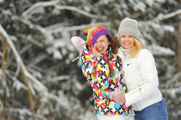 Wall Mural - Two girls in the winter forest emotionally hug and smile.Happy women hug and Express joy