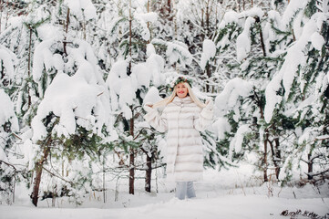 Portrait of a woman in a white fur coat in a cold winter forest. Girl with a wreath on her head in a snow-covered winter forest