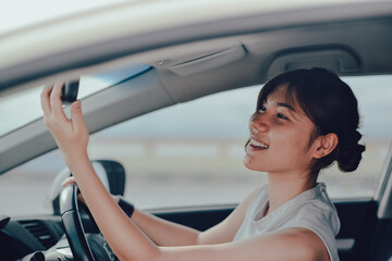 Relaxed asisn woman looking in rear view mirror. siting on the car. lifestyle and people concept.