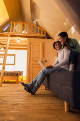 Wall Mural - Cheerful interracial couple using laptop in wooden glamping house