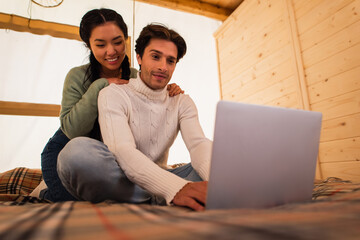 Wall Mural - Young asian woman hugging boyfriend with blurred laptop on bed in glamping house