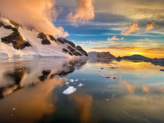 Wall Mural - Beautiful view of snow-covered mountains and a frozen lake under a cloudy sky at sunrise