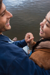 Wall Mural - blurred interracial couple holding hands near lake