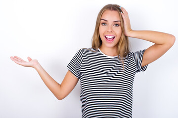 Shocked amazed surprised beautiful blonde girl wearing striped t-shirt on white background hold hand offering proposition