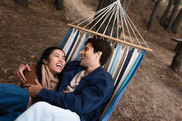 Wall Mural - Excited multiethnic couple hugging in hammock during weekend
