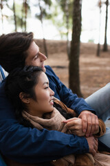 Wall Mural - Side view of interracial couple smiling while hugging in hammock