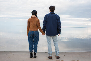 Wall Mural - back view of couple holding hands on shore near sea