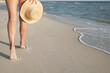 Woman with straw hat walking on beach near sea, closeup