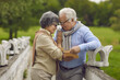 © Studio Romantic - Happy senior couple taking stroll in green park on good summer day. Portrait of cheerful aged man and woman standing on old stone bridge and looking at each other. Relationship, love, respect concept