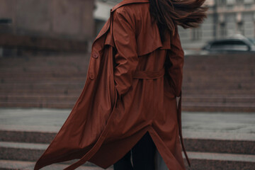 Cropped stylish young woman in fashionable long brown leather coat. Pretty elegant girl model posing. Autumn street style. Casual fashion