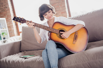 Sticker - Photo portrait young woman playing acoustic guitar sitting on sofa alone at home spending free time