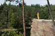 buddhist monk in orange kasaya praying on high rocky cliff over river in forest