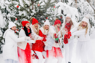 A large group of girls with glasses of champagne in their hands stands in the winter forest.Girls in red and white clothes with new year's drinks in a snow-covered forest.