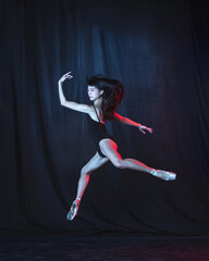 Wall Mural - Young and graceful female ballet dancer in motion isolated on dark background in neon light. Art, motion, action, flexibility, inspiration concept.