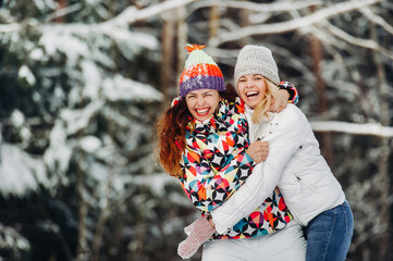 Wall Mural - Two girls in the winter forest emotionally hug and smile.Happy women hug and Express joy