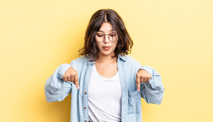 Wall Mural - young pretty girl with open mouth pointing downwards with both hands, looking shocked, amazed and surprised