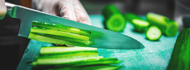 woman chef hands in disposable gloves slicing cucumber on cutting board.