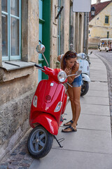 Sticker - A beautiful girl looks in the mirror of a red motor scooter on the street