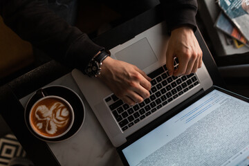 Wall Mural - man with a laptop and coffee works and types on the keyboard indoors. Male hands with luxury watch working in a cafe