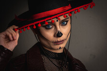 Close-up Portrait Of Calavera Katrina Close Up. Skull Makeup In A Hat On A Gray Background Looking Straight, Serious Look. Dia-de -los -muertos. Day Of Death. Halloween