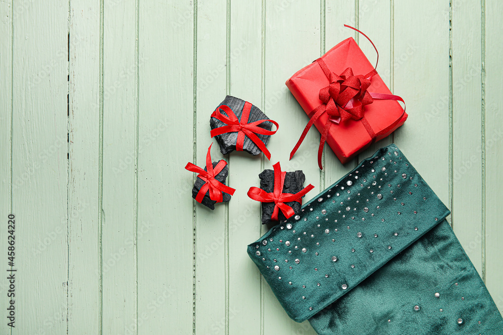 Christmas sock with coal and gift on color wooden background
