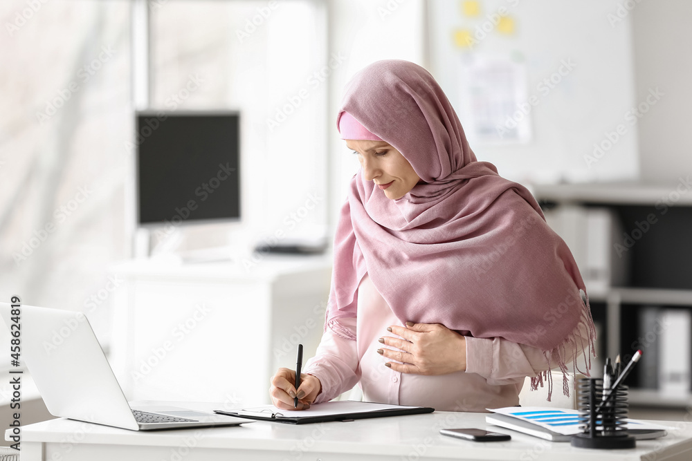 Pregnant Muslim woman working in office