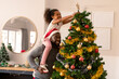 Happy african american father wearing santa hat and daughter decorating christmas tree
