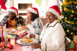 Happy african american grandmother wearing santa hat sitting at christmas table with family