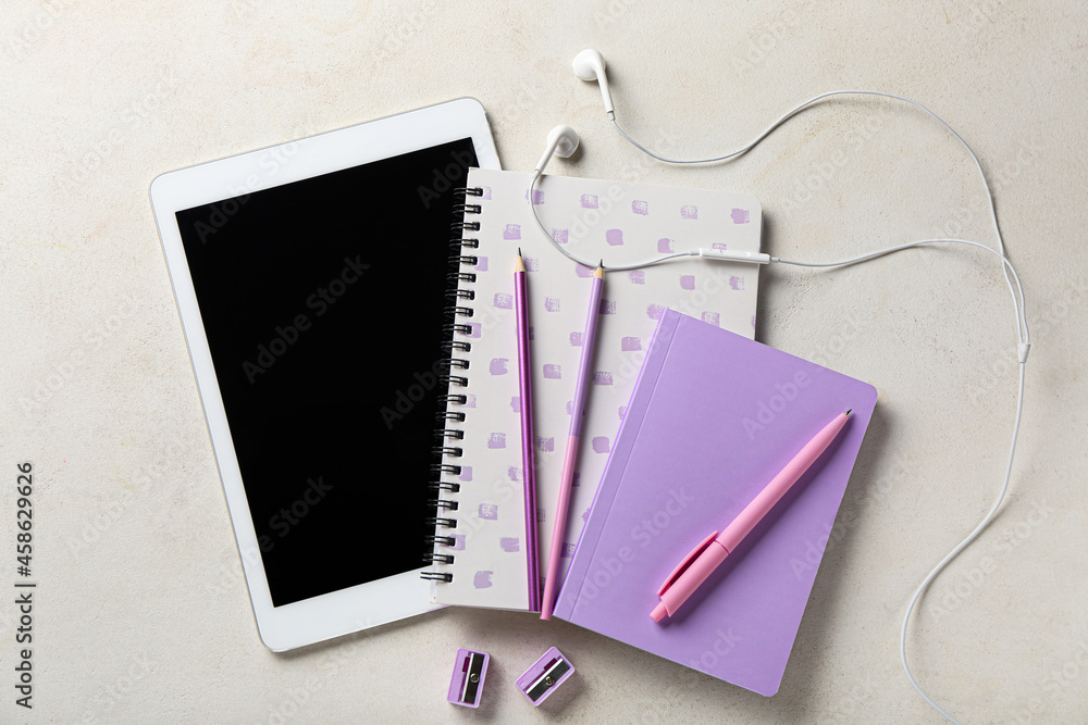 Stationery supplies, tablet computer and earphones on light background