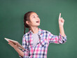 © Tom Wang - Happy student girl holding tablet and pointing upside.Isolated on green chalkboard background..