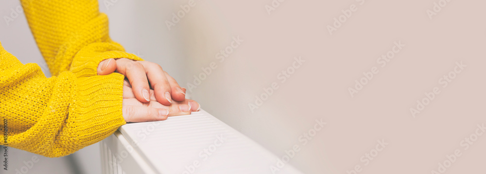 The woman warms her hands on the radiator