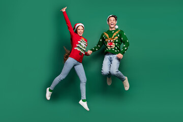 Wall Mural - Photo of inspired funny couple hold hands jump enjoy flight wear ugly sweater isolated green color background