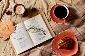 Wall Mural - autumn, season and leisure concept - open book of poems with glasses, cup of coffee, cinnamon bun and candle on warm blankets at home