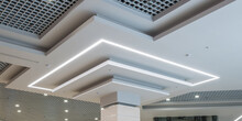 Column In Interior With Suspended And Grid Ceiling With Halogen Spots Lamps And Drywall Construction In Empty Room In Store Or House. Stretch Ceiling White And Complex Shape.
