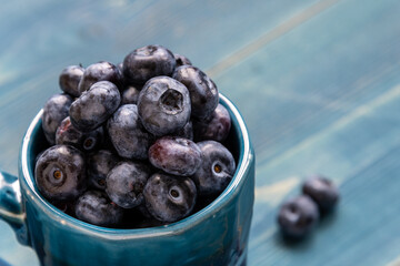 Wall Mural - Ripe juicy blueberries in a cup on a wooden table.