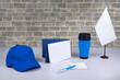 Composition of different promo products with rich colors -Thermo mug, Lanyards Neck Strap, pen,notebook, note pepar, cap. On desk grey and background grey wall