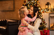 © alones - Pretty young mother woman with little daughter girl in fashionable clothes kiss on the background of christmas decorations and lights. Family winter holidays