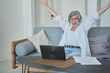 © Justlight - Happy enthusiastic overjoyed senior mature old woman received a joyful letter on laptop. Winning the lottery, sport betting and online casiono, gambling addiction of the elderly.