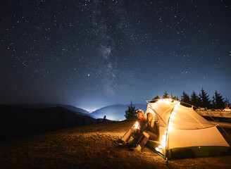 couple sitting down in illuminated tent relaxing after long day of hiking and enjoying the view of e