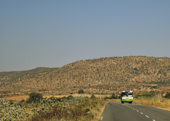 Canvas Print - A Picture of a Bus travelling on an empty highway with Mountains