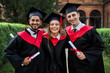 Portrait of three happy smiling graduate friends celebrating graduation in university campus with diploma