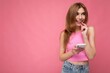 © Ivan Traimak - Photo of good looking young blonde woman wearing pink top poising isolated on pink background with empty space holding in hand and using mobile phone messaging sms looking to the side