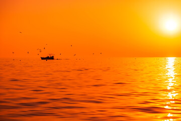 Wall Mural - Bright sunset or sunrise in ocean with fishing boat and seagulls