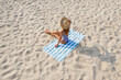 © New Africa - Woman sunbathing on beach towel at sandy coast